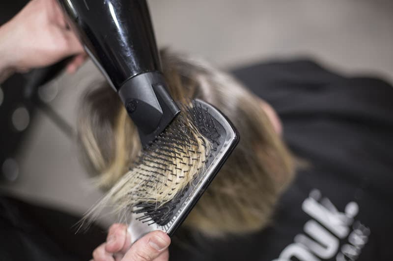 client getting her hair styled with blowdryer and brush by hairdresser