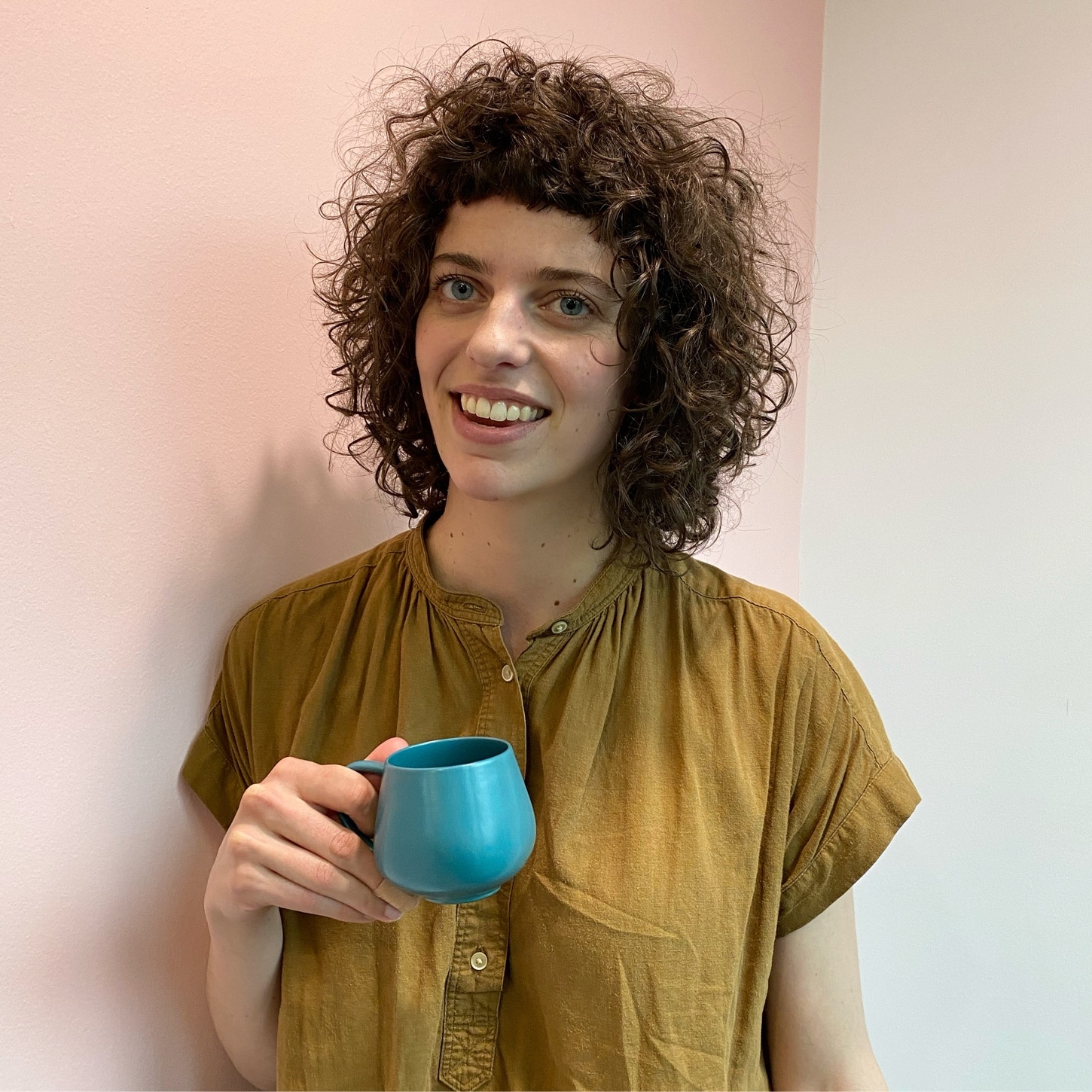 woman holding a blue mug with short curly hair