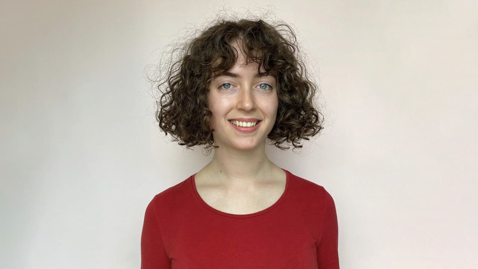 Smiling woman with short defined curly hair on neutral background