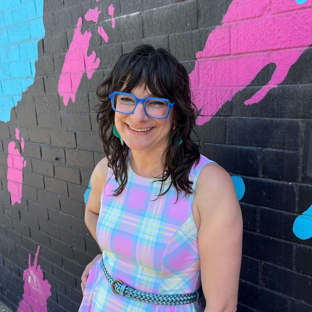 Joi with layered wavy haircut smiling against colourful mural